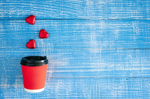 Copo de papel vermelho e doces em forma de coração sobre um fundo de madeira azul