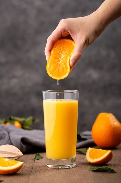 Copo de suco de laranja e uma pessoa espremendo uma laranja nele