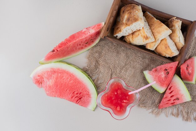 Copo de suco de melancia e cesta de pão na mesa branca.