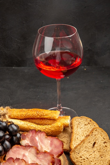 Copo de vinho com pãezinhos e pão na foto de cor escura com álcool.