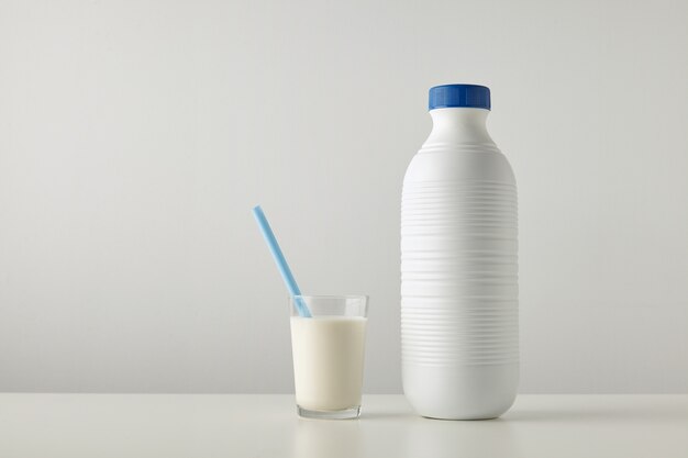 Copo transparente com leite fresco e canudo azul dentro perto de uma garrafa de plástico riffled em branco com tampa azul