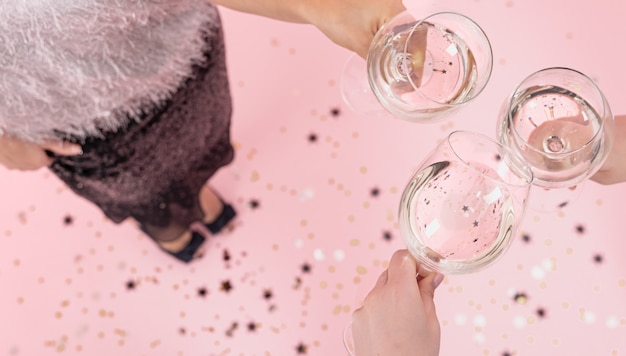 Copos com champanhe nas mãos de meninas em uma festa em um fundo rosa, copie o espaço.