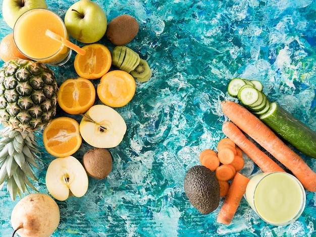 Copos com suco desintoxicante ao lado de frutas e vegetais em fundo de madeira