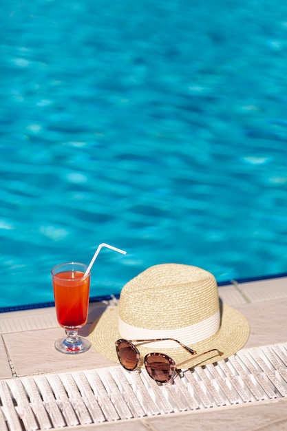 Copos de cocktail e chapéu na margem da piscina