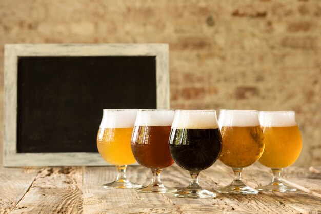 Copos de diferentes tipos de cerveja escura e clara na mesa de madeira em linha