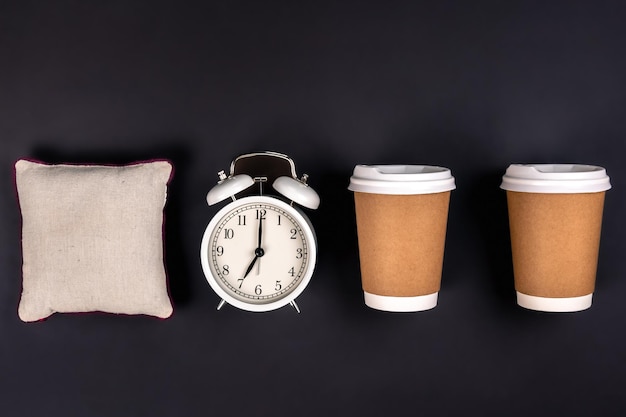 Copos descartáveis de despertador branco e um pequeno travesseiro em um fundo escuro