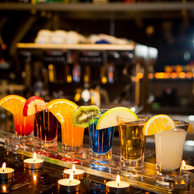 Coquetéis de vista lateral com fatia de limão e kiwi e velas no bar