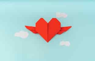 Foto grátis coração origami de papel vermelho com asas e nuvem no fundo azul