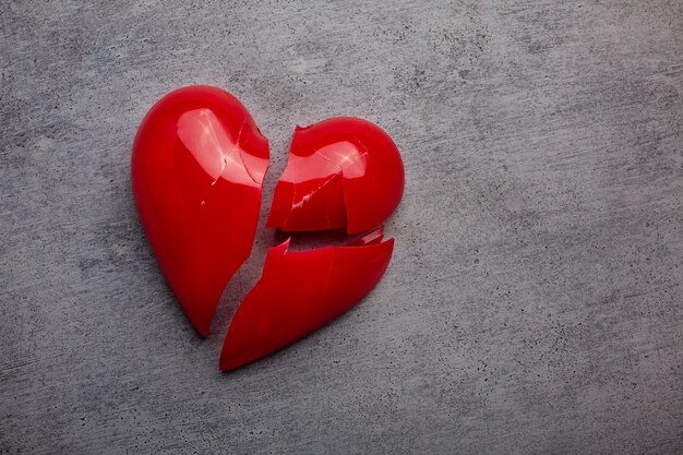 Coração vermelho de plástico quebrado em fundo cinza