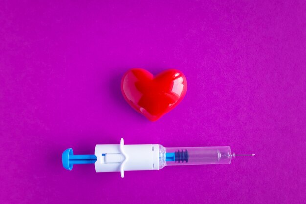 Coração volumétrico com seringas em um fundo rosa. o conceito de apoiar pacientes com doenças cardíacas.