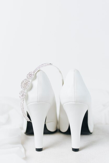 Coroa de diamante sobre o par de saltos altos de casamento branco contra o pano de fundo branco