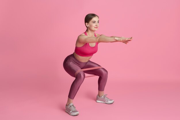 Corpo lento. Bela jovem atleta praticando em estúdio, retrato monocromático rosa.