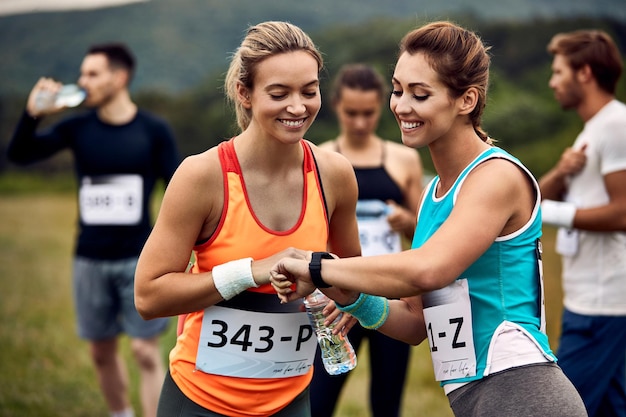 Foto grátis corredor de maratona feliz mostrando relógio inteligente para seu amigo antes da corrida na natureza