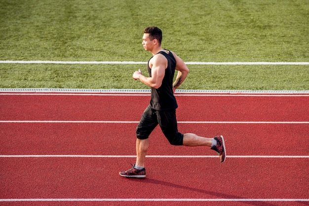 Corredor masculino musculoso correndo na pista de corrida vermelha