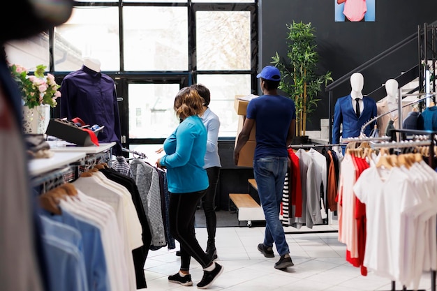 Correio afro-americano segurando pedidos de clientes, saindo do shopping. Homem vestindo uniforme de entrega, preparando-se para enviar pacotes de clientes em uma boutique moderna. Conceito de moda