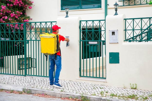 Correio de comida tocando campainha, segurando o tablet, entregando comida na porta. conceito de serviço de envio ou entrega