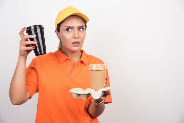 Correio de mulher segurando duas xícaras de café na parede branca.