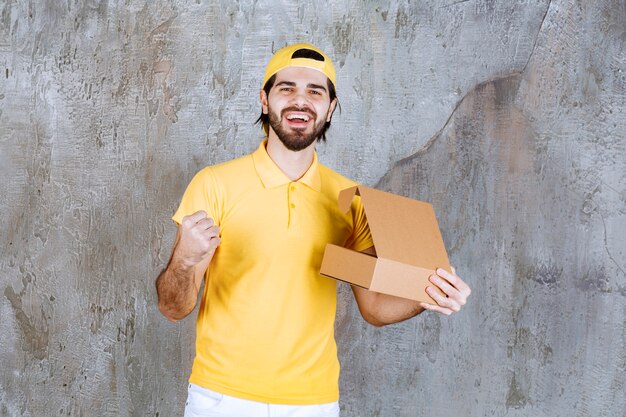 Correio de uniforme amarelo segurando uma caixa de papelão aberta e apreciando o produto