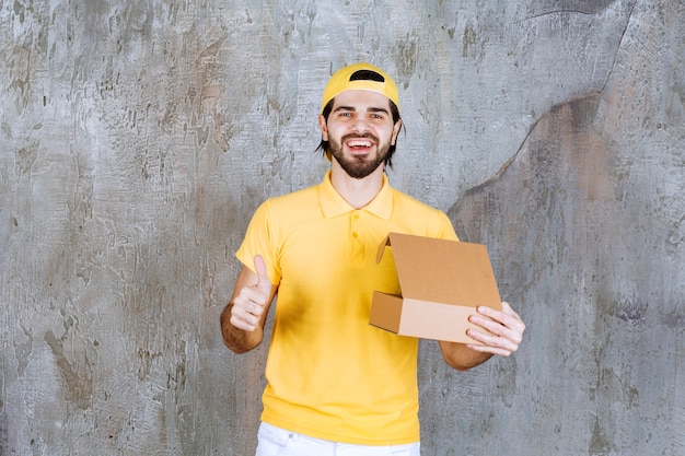 Correio de uniforme amarelo segurando uma caixa de papelão aberta e apreciando o produto