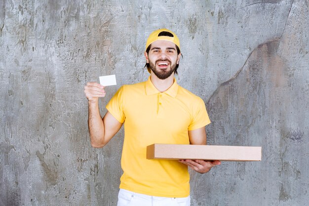 Correio de uniforme amarelo segurando uma caixa de pizza para viagem e apresentando seu cartão de visita.