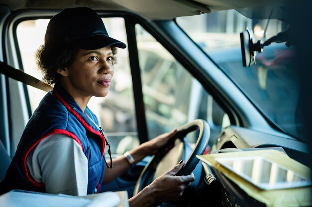 Correio feminino afro-americano dirigindo van de entrega na cidade