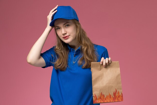 Correio feminino de uniforme azul segurando um pacote de comida na mesa rosa.