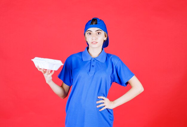 Correio feminino de uniforme azul, segurando uma caixa branca para viagem.