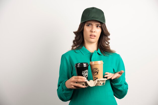Correio feminino de uniforme segurando café para viagem com expressão de loucura.