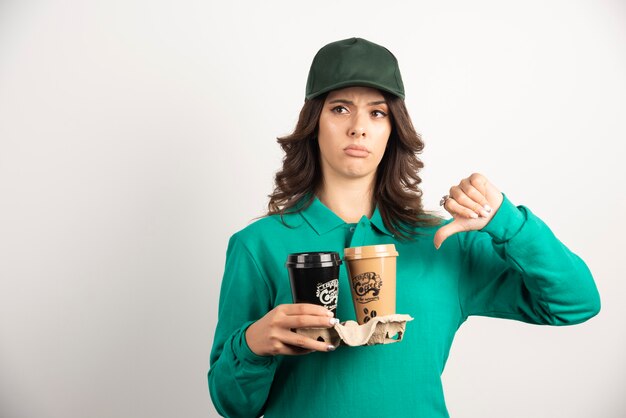 Correio feminino de uniforme segurando café para viagem e mostrando os polegares para baixo.