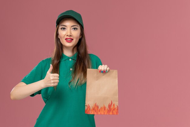 Correio feminino de uniforme verde segurando um pacote de comida na parede rosa.