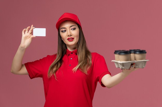 Correio feminino de uniforme vermelho segurando xícaras de café de entrega e cartão no uniforme de empresa de entrega de serviço de vista frontal