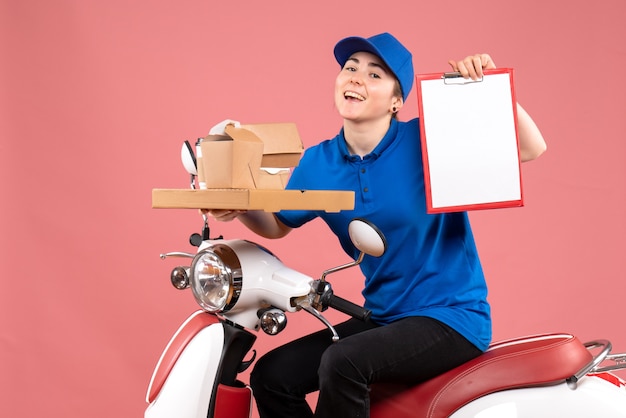 Correio feminino de vista frontal com pacotes de comida e nota de arquivo no serviço de uniforme de bicicleta de entrega de comida de trabalhador cor-de-rosa