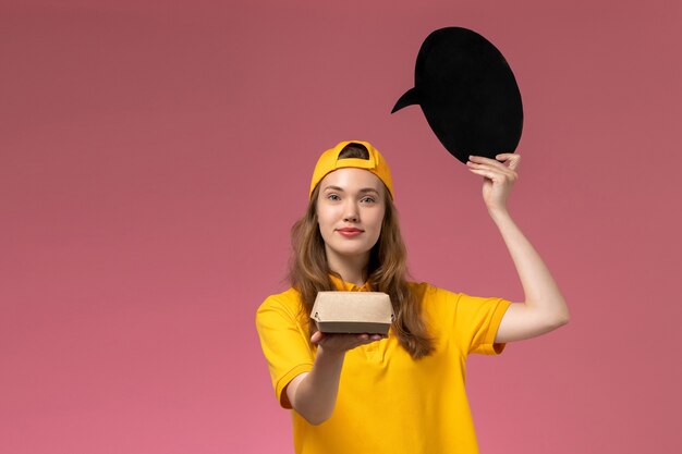 Correio feminino de vista frontal em uniforme amarelo e capa segurando uma placa preta com tigela na parede rosa serviço de entrega uniforme da empresa trabalho