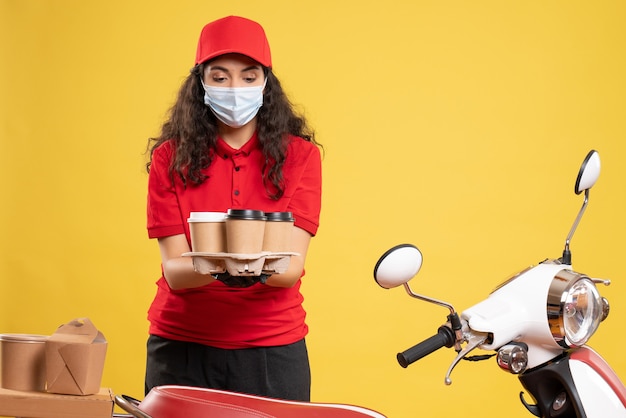 Correio feminino de vista frontal em uniforme vermelho com xícaras de café em fundo amarelo. serviço de uniforme de trabalho pandêmico de entrega de trabalhador