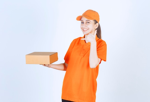 Correio feminino em uniforme amarelo entregando uma caixa de papelão.