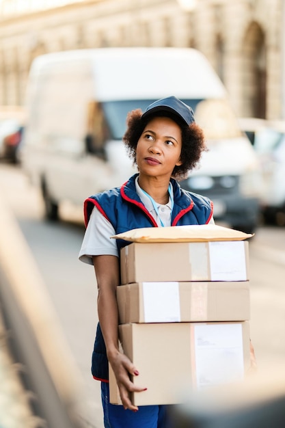 Correio feminino negro carregando pacotes e procurando endereço de entrega na cidade