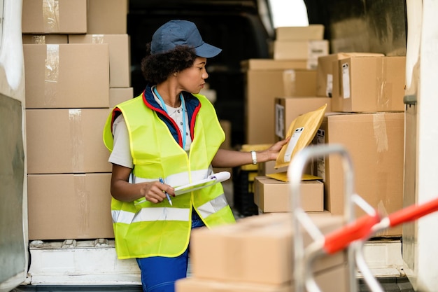 Correio feminino negro trabalhando e verificando pacotes em uma van de entrega