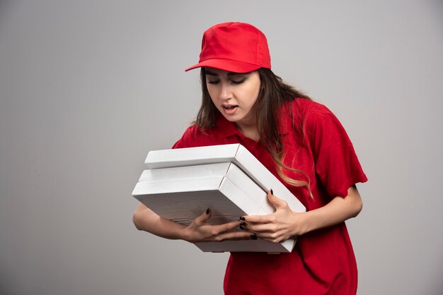 Correio feminino segurando caixas de pizza na parede cinza.