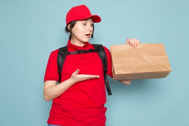 correio jovem polo vermelho boné vermelho mochila preta segurando o pacote surpreso em azul