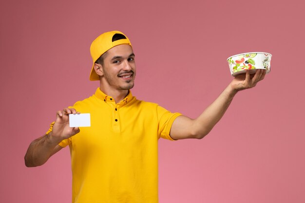 Correio masculino de vista frontal em uniforme amarelo, segurando a tigela de entrega com cartão no fundo rosa.