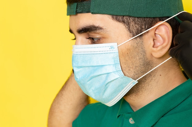 Correio próximo masculino da vista próxima dianteira no tampão verde da camisa verde que veste a máscara estéril