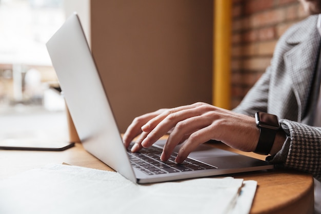 Cortada a imagem do empresário em óculos, sentado junto à mesa no café e usando o computador portátil