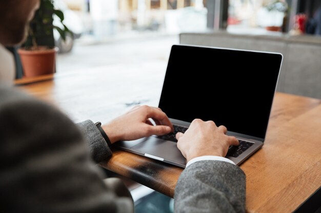 Cortada a imagem do empresário sentado junto à mesa no café e digitando no computador portátil