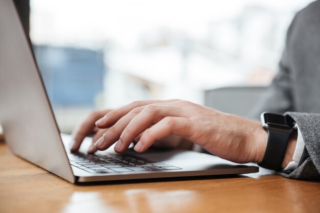 Cortada a imagem do empresário sentado junto à mesa no café e usando o computador portátil