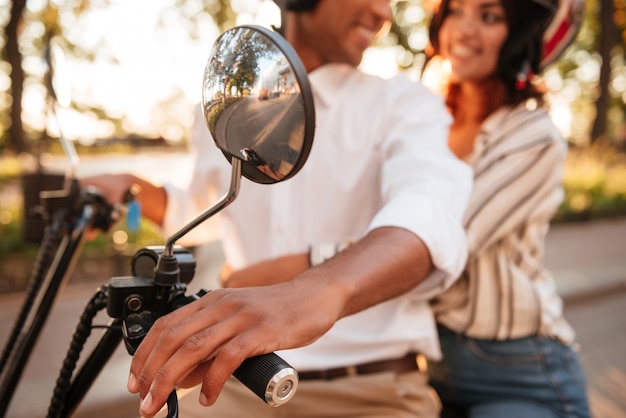 Cortada a imagem do jovem casal Africano passeios de moto moderna no parque e olhando para o outro. Desfocar imagem