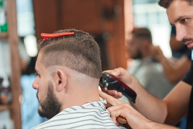 Cortado em close up de um barbeiro profissional trabalhando em sua barbearia, cortando o cabelo de seu cliente.