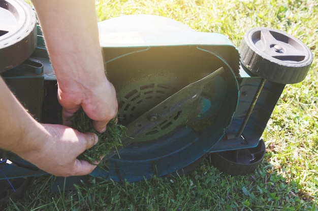 Cortando o cortador de grama elétrico da grama verde. o jardineiro cuida do dispositivo, limpa as facas da sujeira.