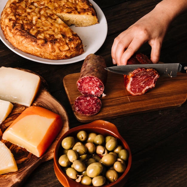 Cortar a mão cortar carne defumada perto de comida sortida