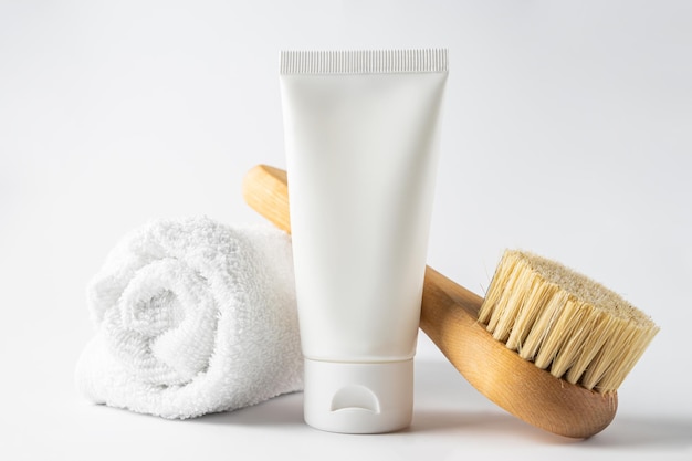 Cosméticos spa, corpo de mulher e produtos para a pele em fundo branco. escova de massagem seca de cerdas naturais e creme corporal ou facial em tubo de plástico branco.