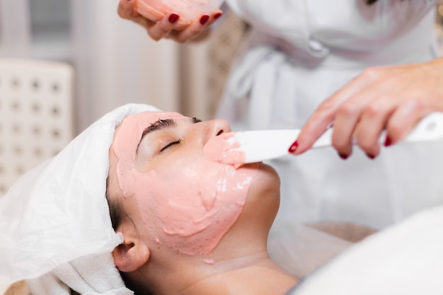 Foto grátis cosmetologista aplica máscara de alginato com espátula no rosto da mulher.